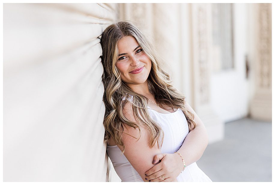 Senior session of girl leaning against white wall at organ pavilion
