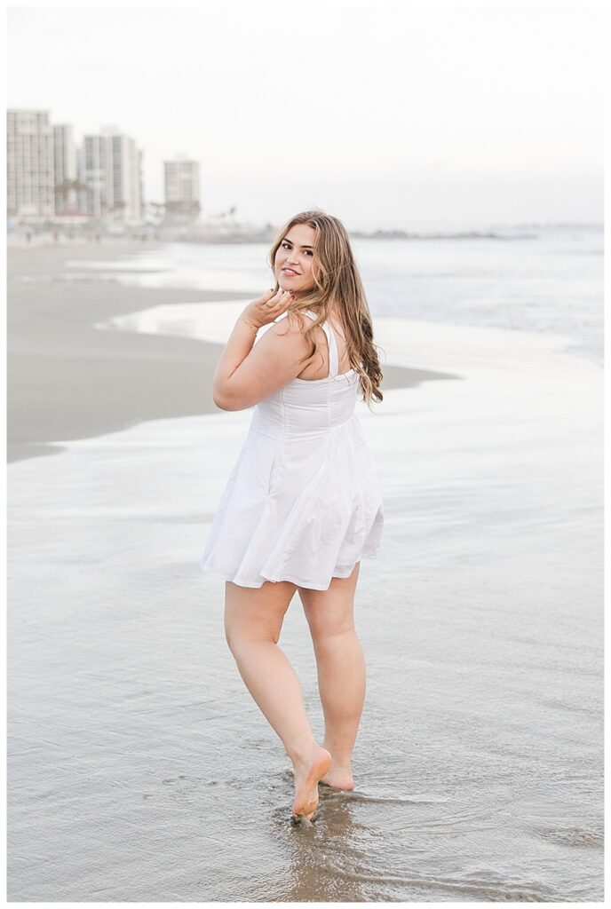 Teen girl in white dress walking away down Coronado Beach