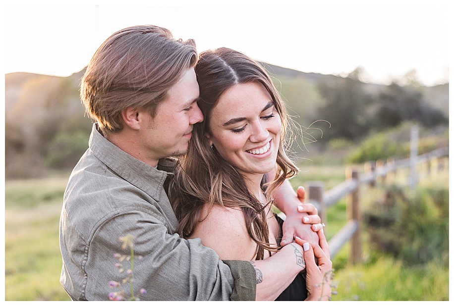 engaged couple hugging and leaning against a wooden fence