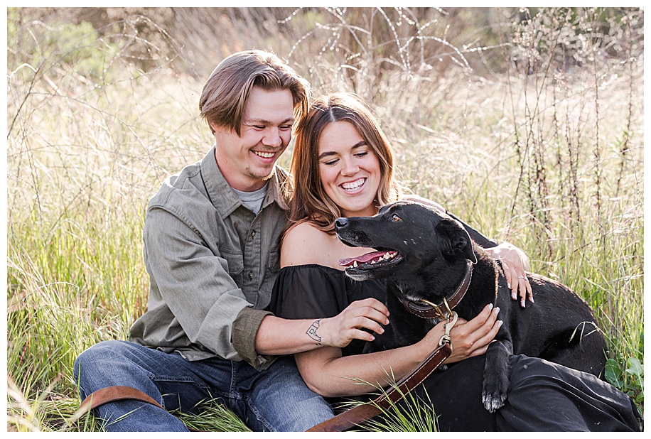 couple sitting in tall grass and playing with their dog