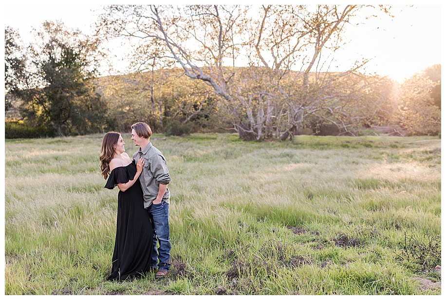 engaged couple lauging in field in front of a tree