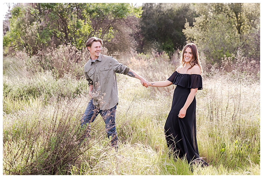 engaged couple walking through tall grass near Sweetwater River Bridge in San Diego