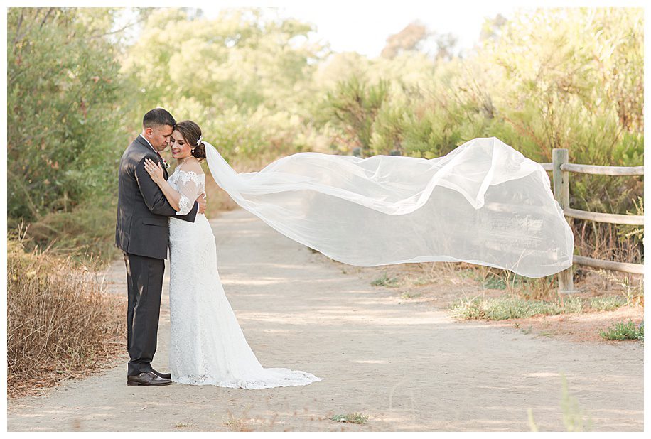 Bride and groom hugging while bride's veil flies in the wind