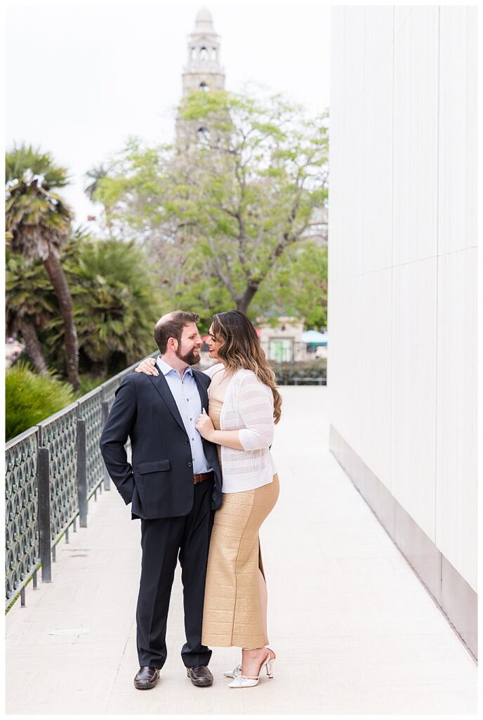 couple by white wall with bell tower in background at Balboa Park San Diego