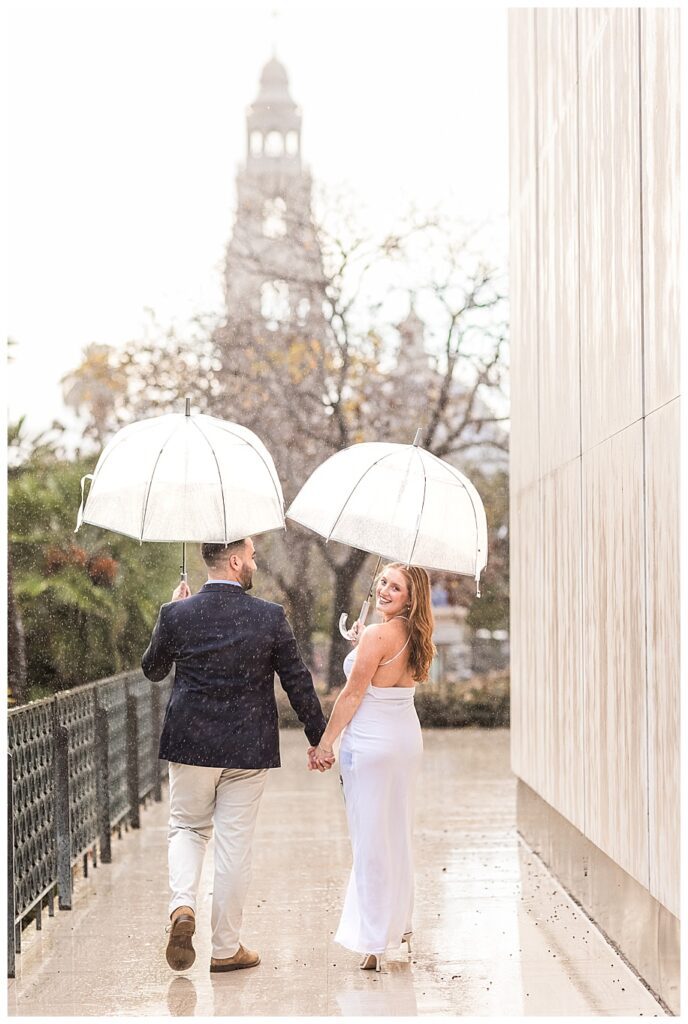 couple walking with umbrellas at balboa park san diego proposal