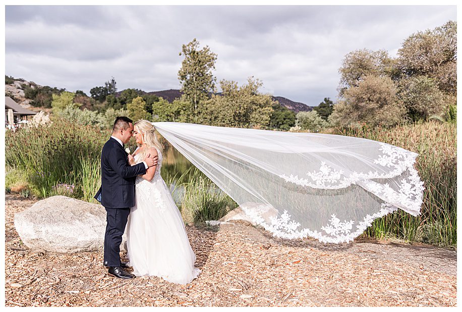 bride and groom hugging with flying veil near pond