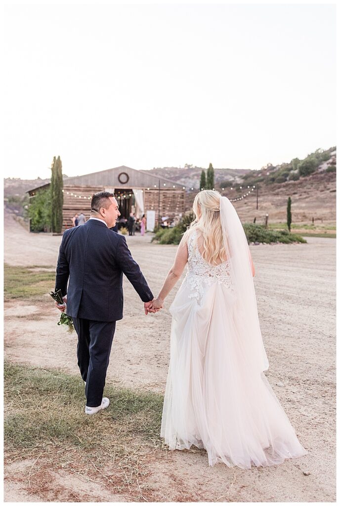 bride and groom walking toward barn reception at their WestWynd Ranch Wedding