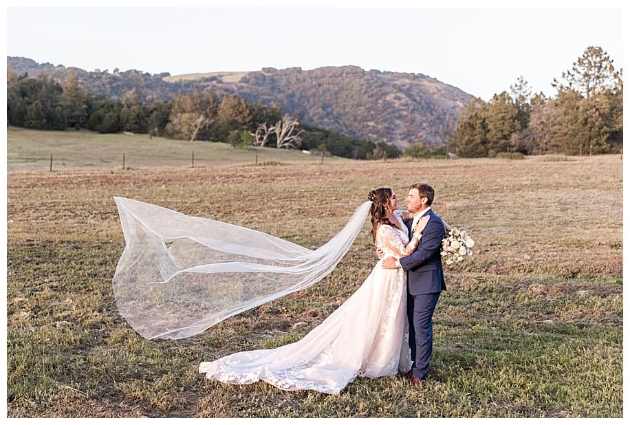 bride and groom on field with veil flying