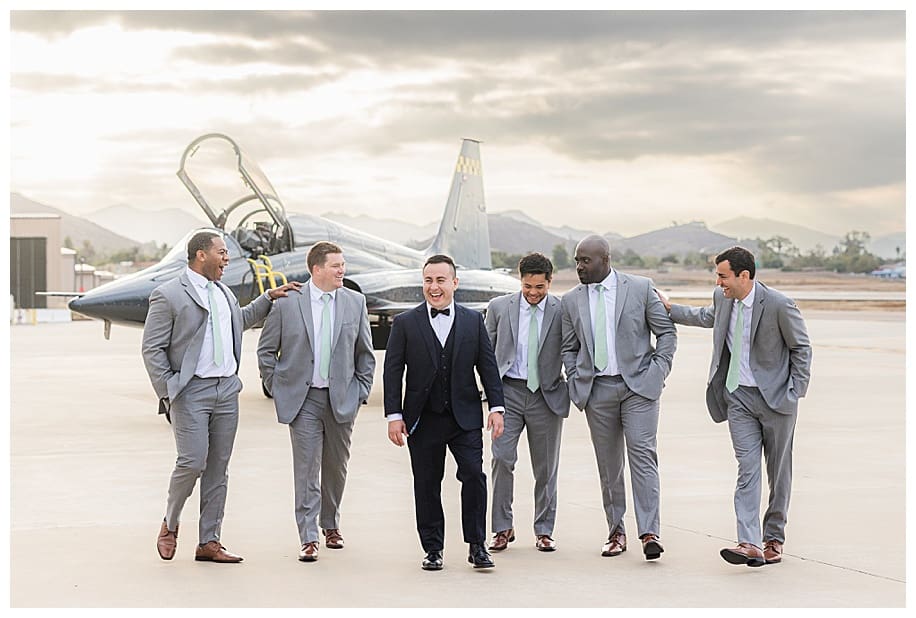 groomsmen and groom standing in front of jet fighter