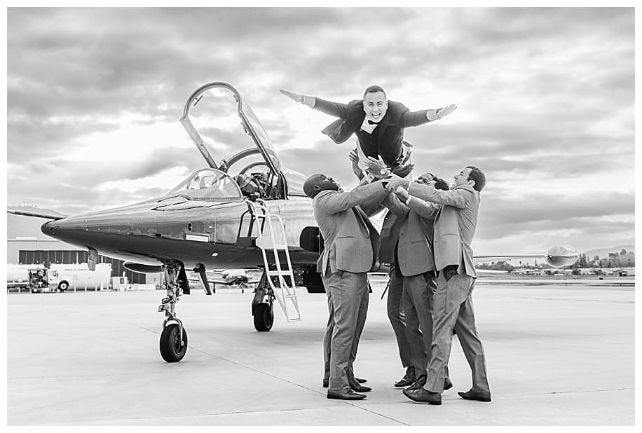 groomsmen tossing groom in air at jet portrait session