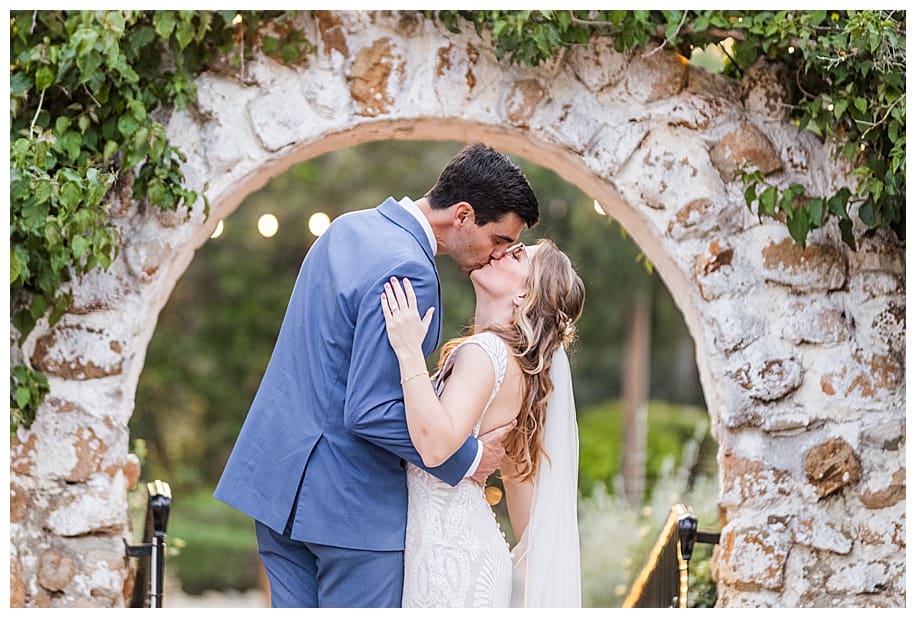 bride and groom kissing under an arch
